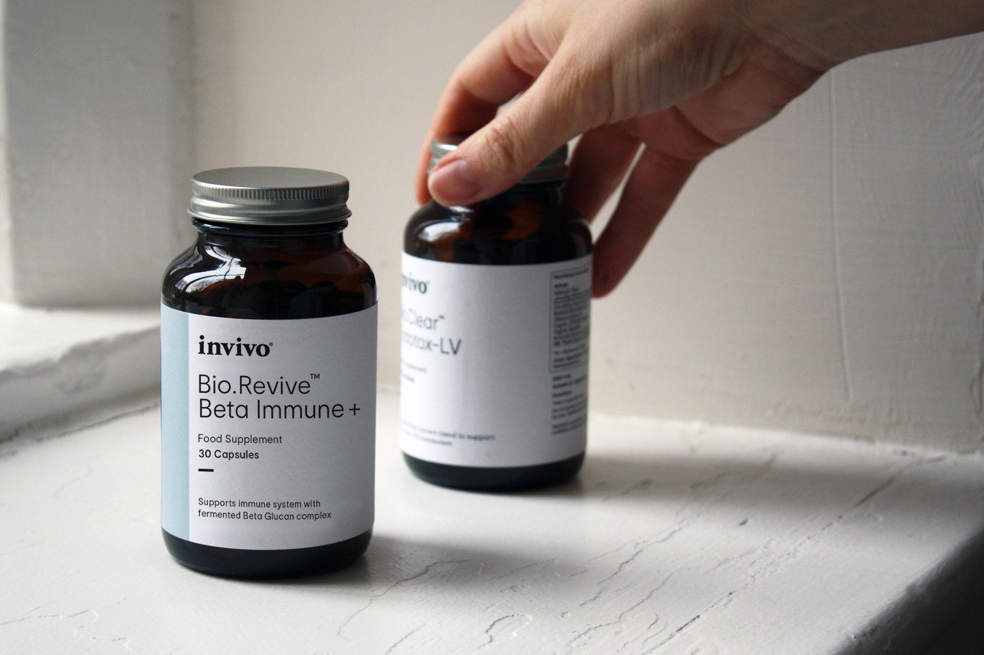 Hand reaching for Invivo Bio.Revive Beta Immune+ bottles