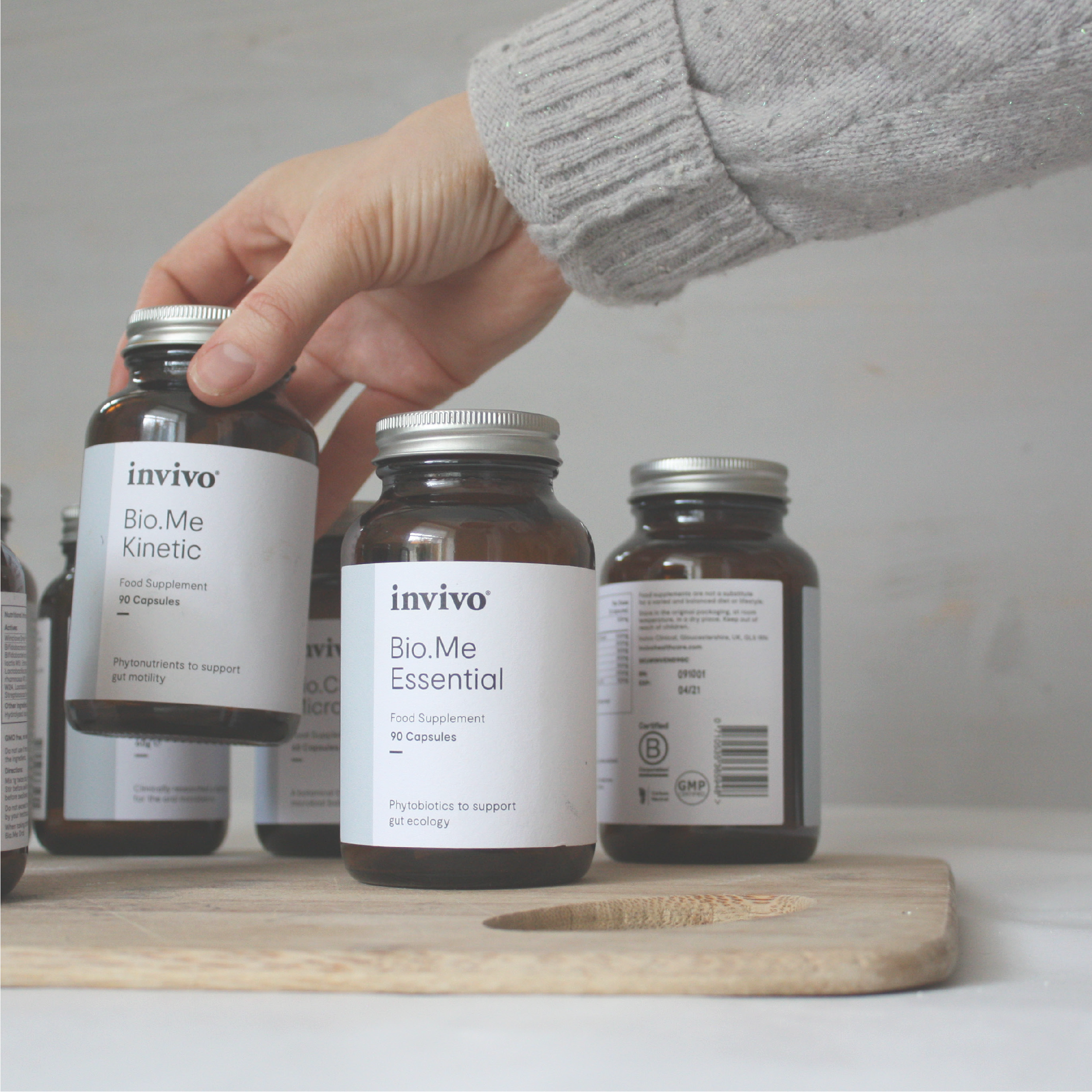 Hand reaching for Invivo Bio.Me supplement bottles on a wooden board