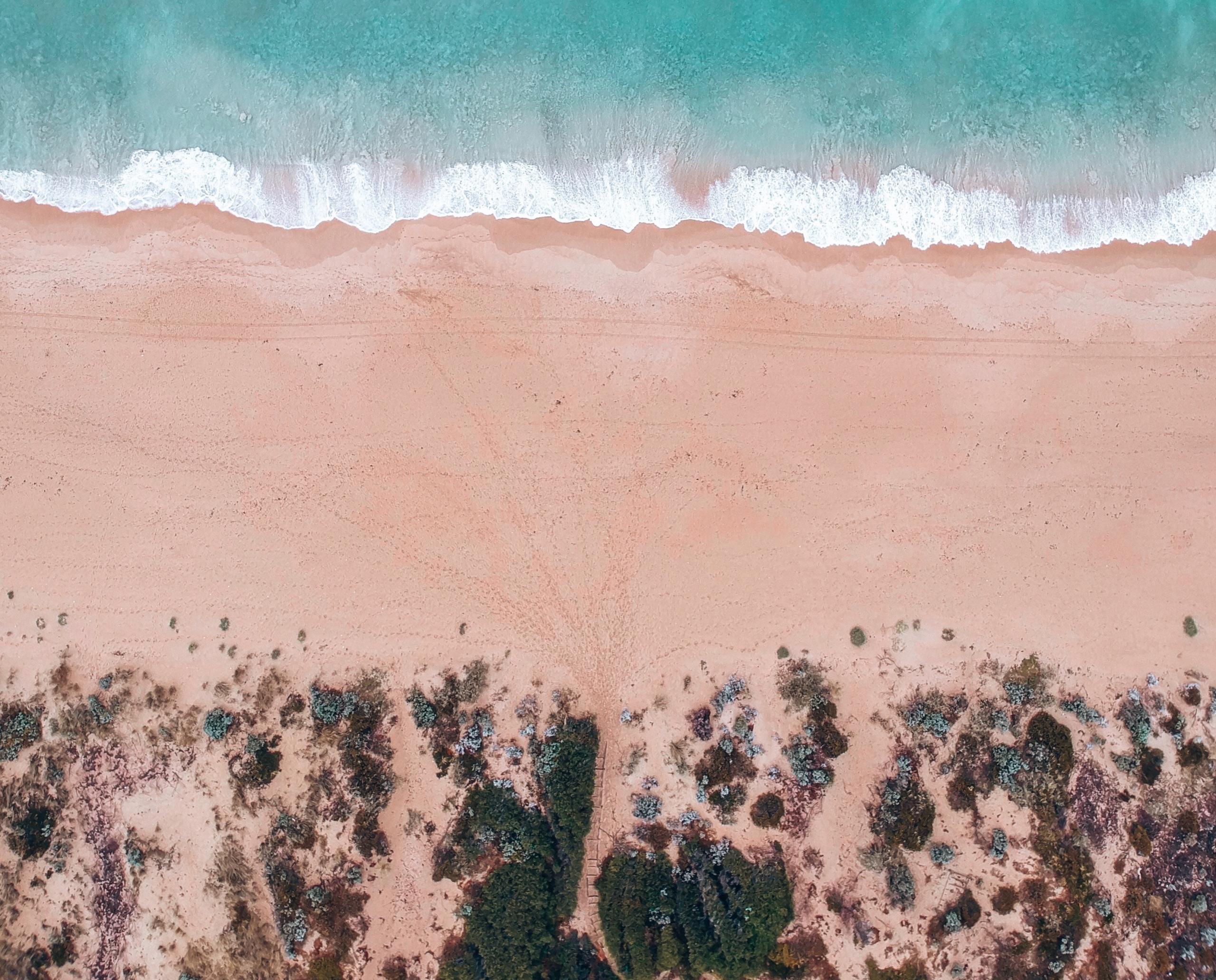 Aerial view of a turquoise coastline meeting pink sand