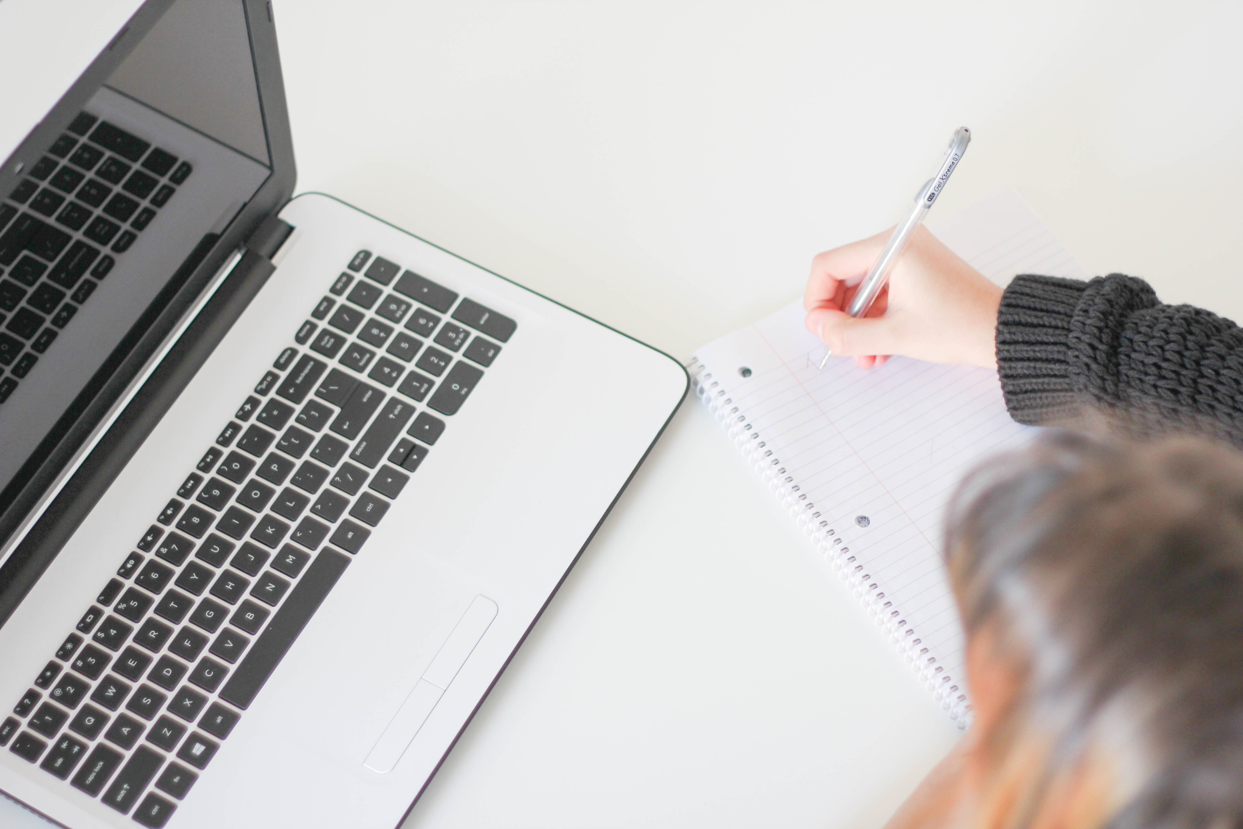 Person writing notes beside a laptop