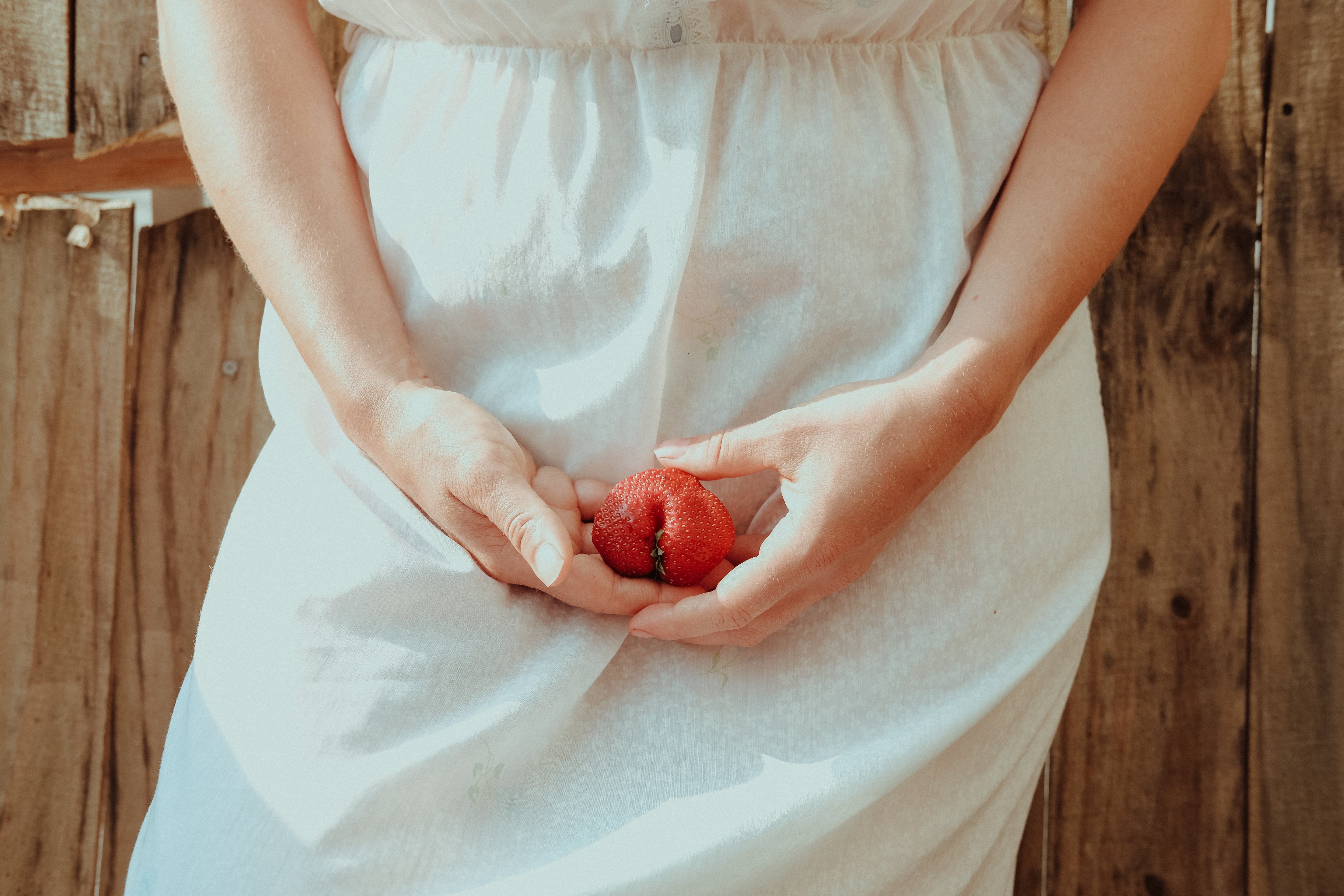 Woman in a white dress holding a pomegranate in front of her abdomen